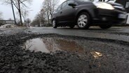 Ein Auto fährt an einem großen Schlagloch vorbei. © dpa Bildfunk Foto: Ingo Wagner