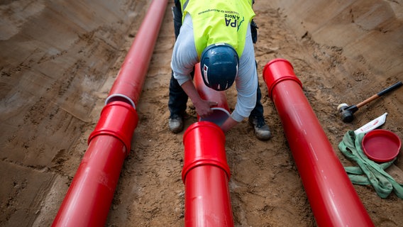 Ein Arbeiter verbindet zwei Kabelschutzrohre in einem Kanal der Erdkabeltrasse A-Nord in Rhede. © DPA Foto: Fabian Strauch