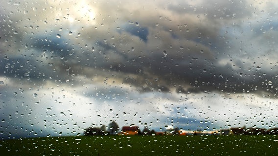Durch eine mit Regen benetzte Autoscheibe sind dunkle Wolken zu sehen. © dpa-Bildfunk Foto: Arno Burgi