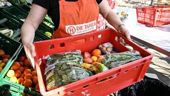 Eine Mitarbeiterin der Tafeln hält eine Kiste mit Obst und Gemüse in die Kamera. © picture alliance/dpa | Felix Kästle Foto: Felix Kästle