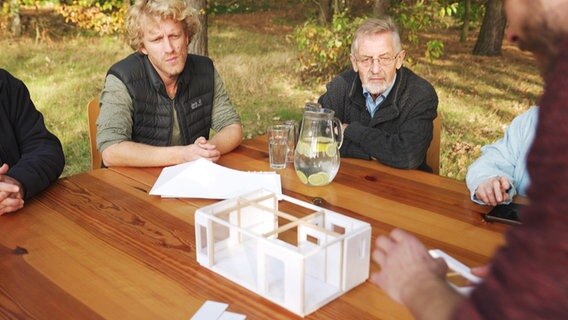 Junge und ältere Menschen sitzen an einem Tisch, auf dem einModell eines Tiny Houses steht. © NDR 