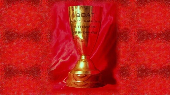 Der Pokal eines Musiker-Wettkampfs steht auf einem roten Hintergrund. © NDR Foto: Harry Houben