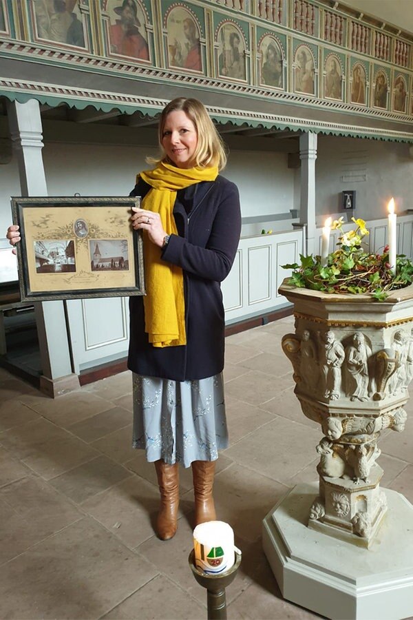 Eine Frau steht in einer Kirche und hält gerahmte Fotos in der Hand. © NDR Foto: Ines Krawinkel
