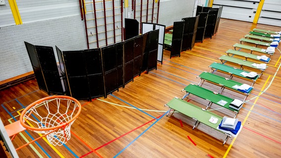 In einer Turnhalle sind Behelfsbetten und Trennwände  aufgestellt. © picture alliance Foto: Robin Utrecht