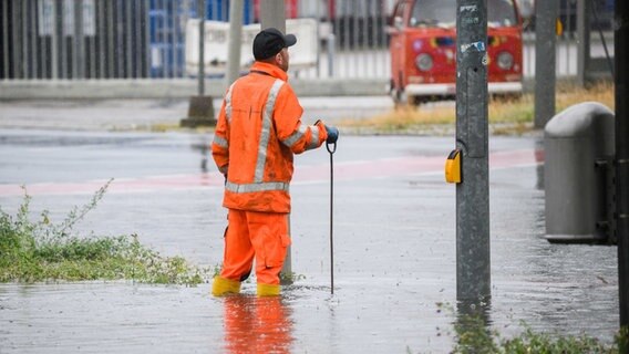 Ein Mitarbeiter der Stadtentwässerung der Stadt Hannover steht auf der überfluteten Hermesallee am Messegelände. © ulian Stratenschulte/dpa 