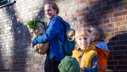 Ein Vater und seine zwei Kinder tragen den Einkauf nach Hause und lächeln dabei in die Kamera. © picture alliance 