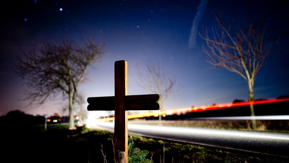 Ein Kreuz steht am Rand einer Landstraße, dahinter vorbeifahrende Autos und der Nachthimmel © dpa-Bildfunk / picture-alliance Foto: Julian Stratenschulte