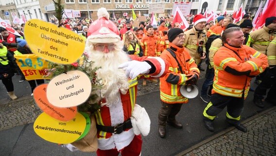 Ein Feuerwehrmann mit Tarifforderungen an einem Weihnachtsbaum und weitere Beschäftige im öffentlichen Dienst stehen bei einem Warnstreik vor dem niedersächsischen Finanzministerium. © dpa 
