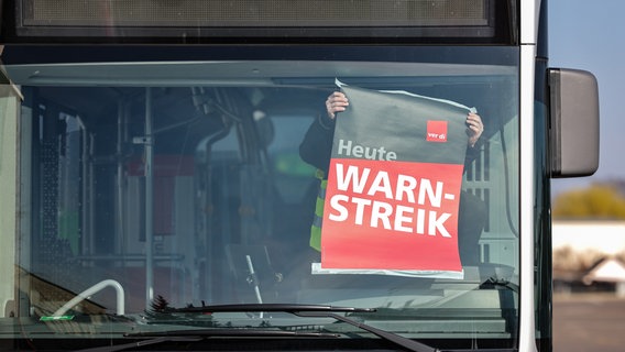 Ein Mitarbeiter befestigt ein Warnstreik-Plakat in einem Bus an der Frontscheibe. © picture alliance/dpa Foto: Jan Woitas