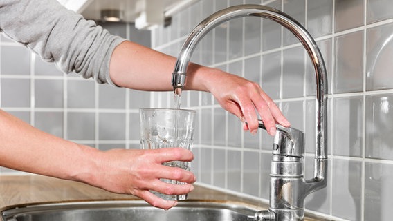 Ein Mensch füllt ein Glas Wasser an einem Wasserhahn. © Imago Images 