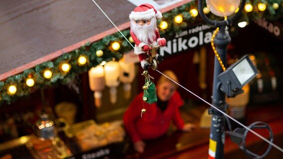 Ein radelnder kleiner Weihnachtsmann bewegt sich auf einem Seil über den Köpfen der Besucher auf dem Weihnachtsmarkt. © picture alliance/dpa/Friso Gentsch Foto: Friso Gentsch