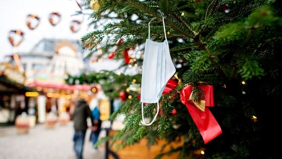Eine gebrauchte medizinische Maske hängt an einem Weihnachtsbaum auf dem einem Weihnachtsmarkt. © picture alliance/dpa Foto: picture alliance/dpa | Hauke-Christian Dittrich