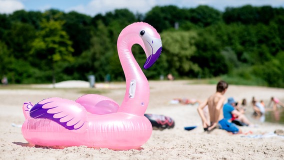 Ein aufblasbares Schwimmtier in Form eines Flamingos liegt bei sommerlichen Temperaturen im Sand an einem Badesee im Ortsteil Neermoor. © picture alliance Foto: Hauke-Christian Dittrich