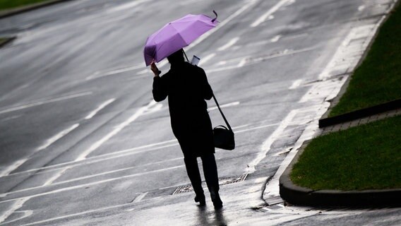 Eine Frau geht bei stürmischen und regnerischen Wetter mit einem Regenschirm über eine Straße. © picture alliance/dpa/Julian Stratenschulte Foto: Julian Stratenschulte