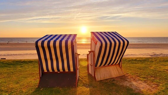 Die Sonne geht zwischen zwei Strandkörben auf Norderney unter. © NDR Foto: Marion Holtz