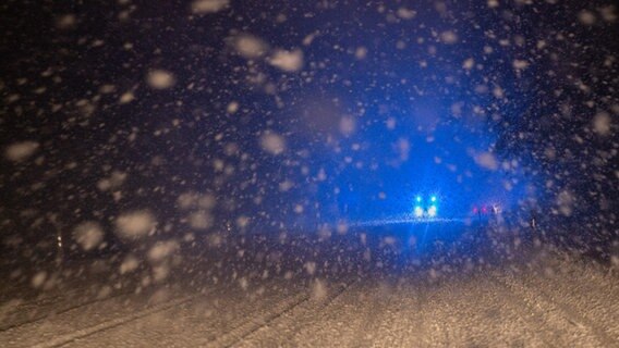 Im dichten Schneetreiben fährt ein Wagen mit Blaulicht auf einer schneebedeckten Straße. © picture alliance/dpa Foto: Bernd Weißbrod