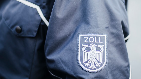 Auf dem Ärmel einer blauen Uniform steht das Wort Zoll und der Bundesadler ist abgebildet. © NDR Foto: Julius Matuschik