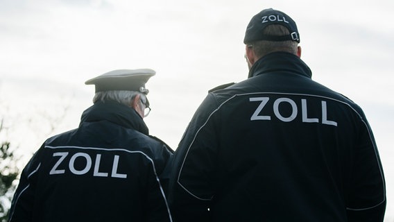 Zwei Männer tragen eine blaue Uniform mit der Aufschrift Zoll auf dem Rücken. © NDR Foto: Julius Matuschik