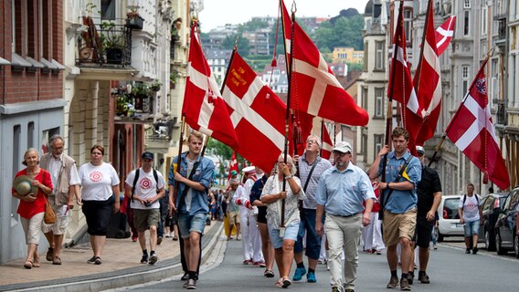 Fahnenträger führen den Umzug durch die Innenstadt beim Jahrestreffen der dänischen Minderheit an. Das Jahrestreffen - dänisch Arsmöde - wurde zum ersten Mal 1921 gefeiert, ein Jahr nach der Volksabstimmung und Grenzziehung von 1920. © picture alliance/Axel Heimken/dpa Foto: Axel Heimken