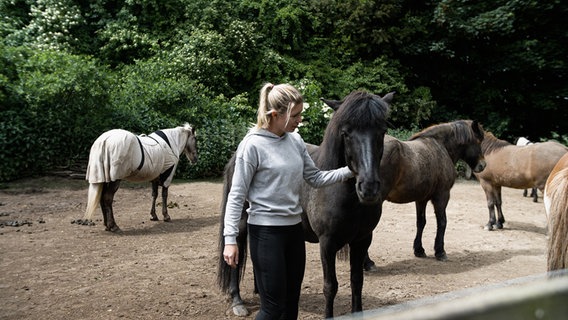 Die Hofbetreiberin streichelt ein Pferd, mehrere Pferde stehen im Hintergrund © NDR Foto: Dominik Dührsen