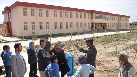 Eine Gruppe von Menschen stehen vor einer afghanischen Schule und unterhalten sich.  Foto: Marga Flader