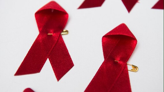 Viele rote Schleifen, das weltweit anerkannte Symbol für die Solidarität mit HIV-Infizierten, liegen am Welt-Aids-Tag auf einem Tisch. © Lukas Schulze/dpa Foto: Lukas Schulze/dpa
