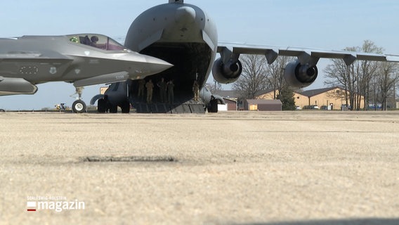 Auf einem militärischem Flugplatz stehen ein Transporter und ein Kampfjet. © NDR 