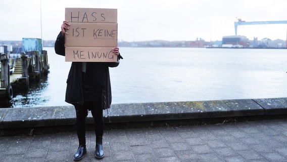 Eine Frau steht an der Kiellinie und hält ein Schild mit der Aufschrift "Hass ist keine Meinung" vor ihr Gesicht. © NDR Foto: Lisa Pandelaki