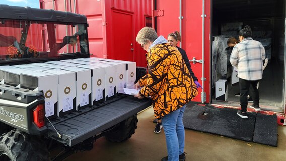 Christine Stoecklein steht vor einem mit Kartons beladenen Fahrzeug und schaut in eine Bestellliste. Christine Stoecklein steht vor einem mit Kartons beladenen Fahrzeug und schaut in eine Bestellliste. © Christine und Edmund Stoecklein