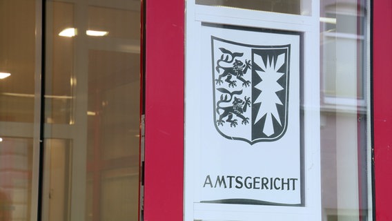 Ein weißes Schild mit schleswig-holsteinischem Wappen und Schriftzug Amtsgericht hängt an der verglasten Eingangstür des Amtsgerichts Itzehoe © NDR 