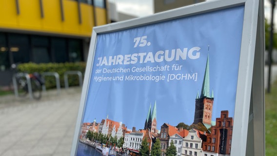 Auf einem Aufsteller steht: "75. Jahrestagung der Deutschen Gesellschaft für Hygiene und Mikrobiologie (DGHM)" © NDR Foto: Margarita Ilieva