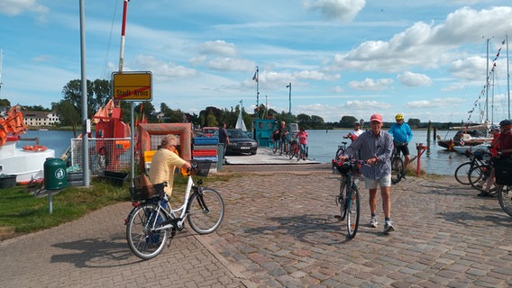 Einige Menschen, die Fahrräder schieben, befinden sich am Hafen von Arnis an der Schlei. © NDR Foto: Lukas Knauer