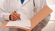 Arzt in weißem Kittel und mit Stethoskop schreibt etwa auf ein Blatt in einem Ordner. © imageBROKER/josexhernandez Foto: jose hernandez