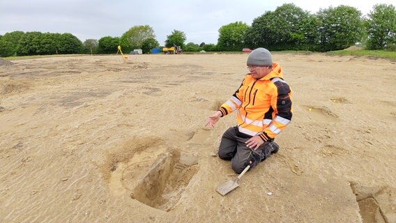 Ein Mann kniet vor einer Grabungsstelle. © NDR Foto: Peer-Axel Kroeske