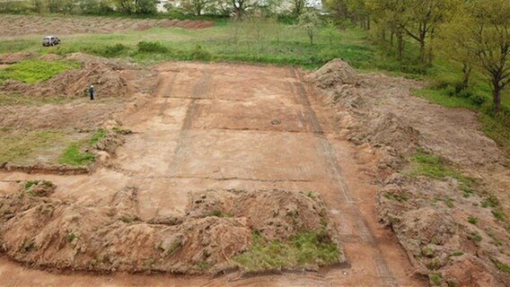 Aus der Luft sind auf einer Fläche mit Erdboden dunkle Linien zu erkennen, die parallel verlaufen. Aus der Luft sind auf einer Fläche mit Erdboden dunkle Linien zu erkennen, die parallel verlaufen. © Archäologisches Landesamt SH