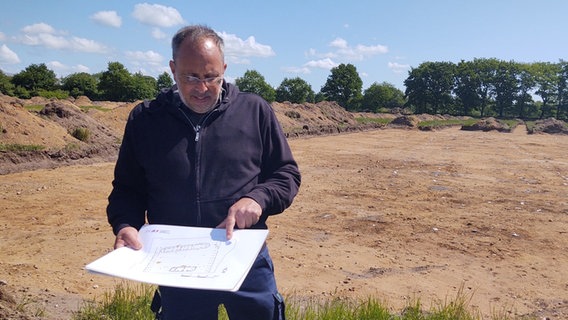 Alexander Maaß steht mit einem Grundrissplan vor der freigelegten Fläche. © NDR Foto: Peer-Axel Kroeske