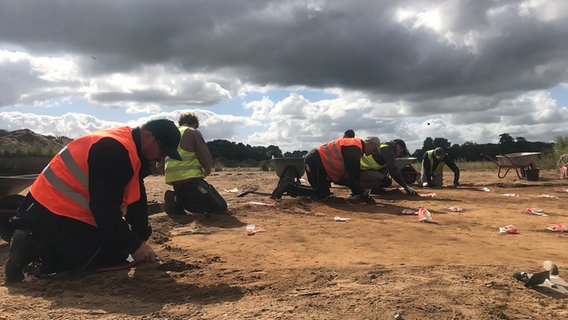Archäologen sitzen auf dem Boden bei Grabungsarbeiten auf dem Northvolt-Gelände in Heide. © NDR Foto: Sven Jachmann