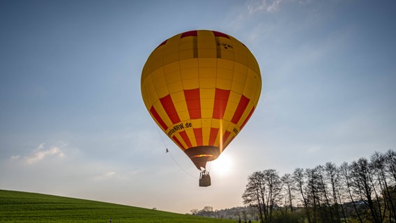 Ein Heißluftballon fliegt über einem Feld, während die Sonne untergeht. © IMAGO Foto: Markus Klümper