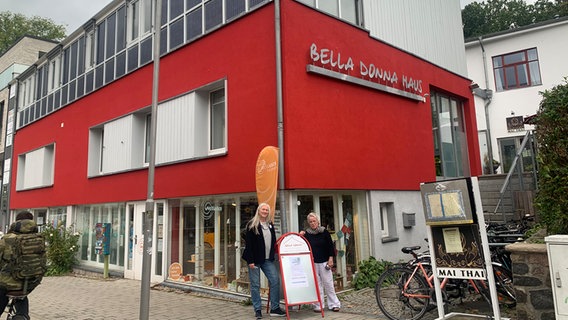 Zwei Frauen stehen hinter einem Aufsteller, im Hintergrund steht das Bella Donna Haus in Bad Oldesloe © NDR Foto: Corinna Below