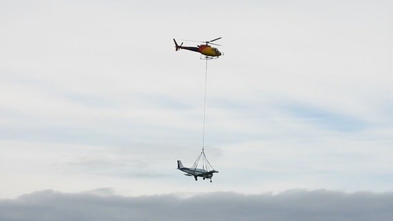 An einem Hubschrauber hängt ein geborgendes Flugzeug. © NDR 
