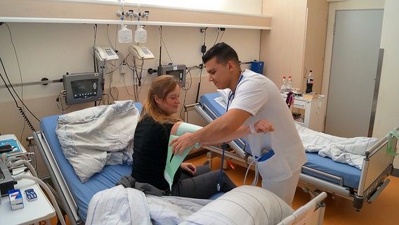 Mohammad Berri legt in einem Krankenhauszimmer einer Patientin eine grüne Manschette um. © NDR Foto: Kai Salander