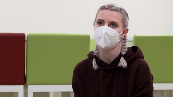 Eine junge, blonde Frau mit Zöpfen steht mit einem Mundschutz in einem Raum. © NDR 