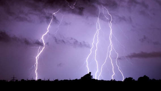 Mehrere Blitze bewegen sich vor einem lila Himmel in richtung Erdoberfläche © picture alliance Foto: Julian Stratenschulte