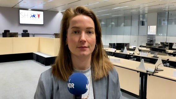 NDR-Reporterin Hannah Böhme steht in einem Gerichtssaal in Utzehoe mit einem Mikrofon in der Hand und blickt in die Kamera. © NDR 