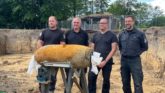 Specjaliści z Explosive Ordnance Disposal Service pozują do kamery z rozbrojoną bombą powietrzną na zawiasie.  © NTR Zdjęcie: Christian Nagel