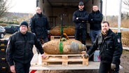 Einsatzkräfte des Kampfmittelräumdienstes zeigen sich mit mehreren entschäften Bomben. © dpa Foto: Daniel Bockwoldt