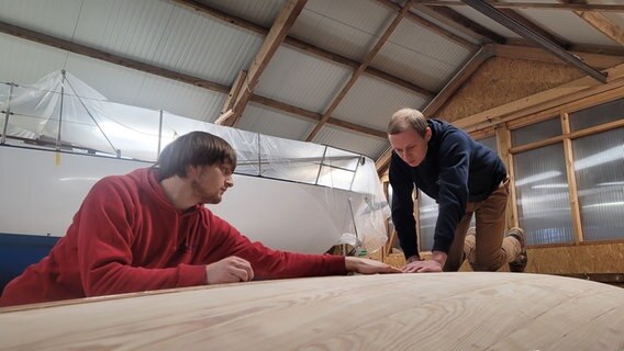 Zwei Männer arbeiten zusammen an einem Boot. © NDR Foto: Frank Goldenstein