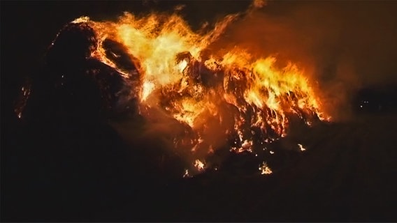 Ein Berg von Strohballen steht nachts hell in Flammen © NDR 