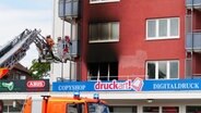 Nach einem Wohnungsbrand am Exerzierplatz in Kiel sind Einsatzkräfte auf einer Löschleiter vor dem Fenster zu sehen © Daniel Friedrichs Foto: Daniel Friedrichs