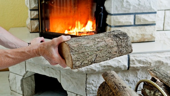 Eine Person legt einen Holzscheit in einem brennenden Kamin nach © picture alliance / dpa Themendienst Foto: Monique Wüstenhagen